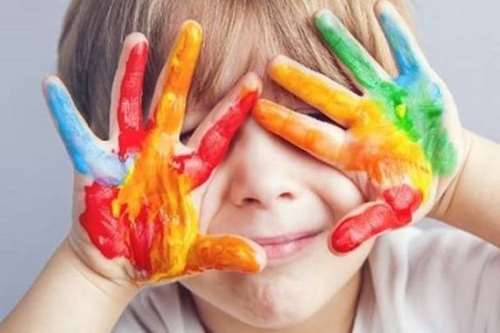 Foto di un bambino con le mani colorate di tutti i colori davanti agli occhi