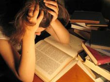 immagine di una studentessa che legge un volume con le mani nei capelli, circondata da tanti libri