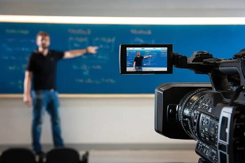 Immagine di una videocamera in primo piano che riprende una lezione sullo sfondo