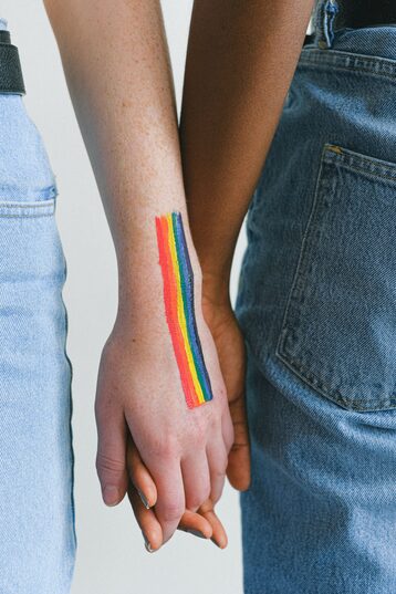 Due persone che si tengono per mano e sulla mano hanno un arcobaleno