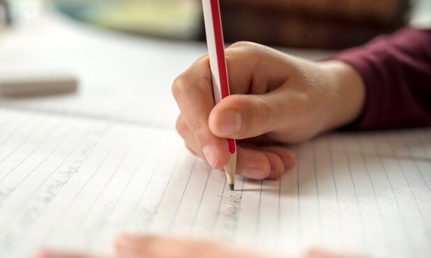 Foto di una mano che scrive su un quaderno a matita
