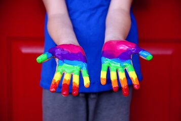 Persona che mostra le mani colorate con la pittura rainbow