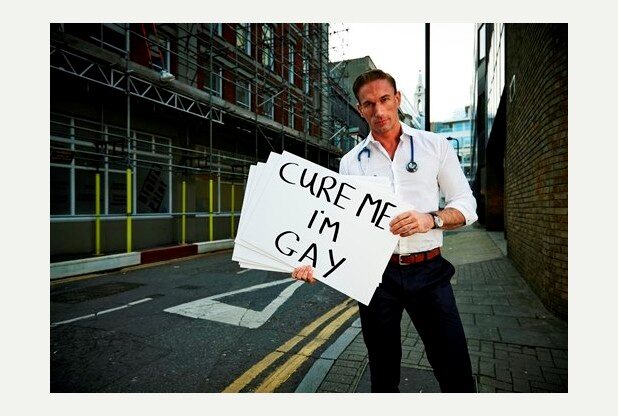 Un uomo con lo stetoscopio e un cartello in mano, recante la scritta "cure me, I'm gay"